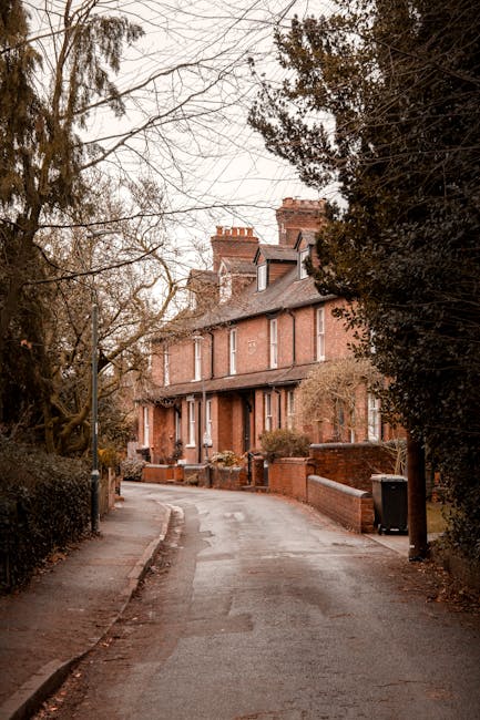 Image depicting a row of Victorian-style terraced houses with ornate ironwork balconies and bay windows, built with brick and painted in shades of white and pastel blue. The houses are situated behind